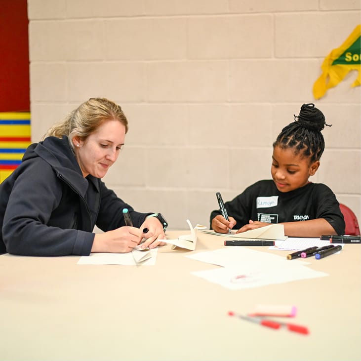 Photo of a lady and a child writing or drawing at a table